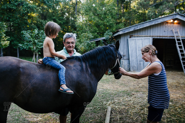 A young child sits on a pony as her grandmother and grandfather hold the horse