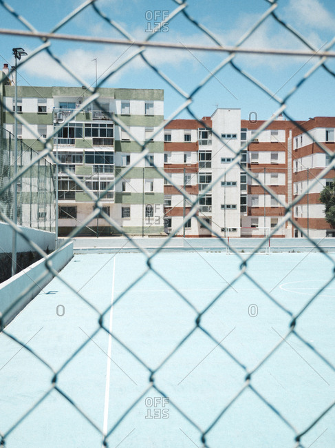 Blue football soccer court through fence with buildings in background