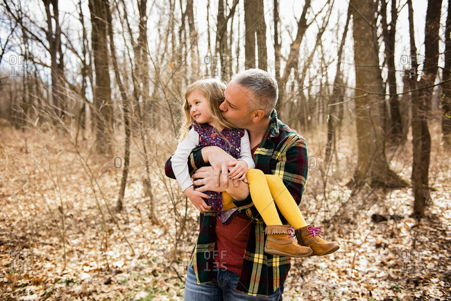 Loving father holds and kisses smiling daughter on cheek in Fall woods