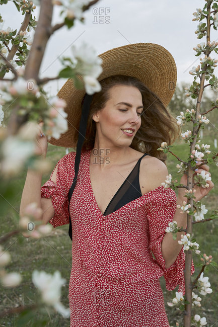 Happy cute beautiful woman smiling in a dress in a wicker hat stands background of flowers of apple tree branches