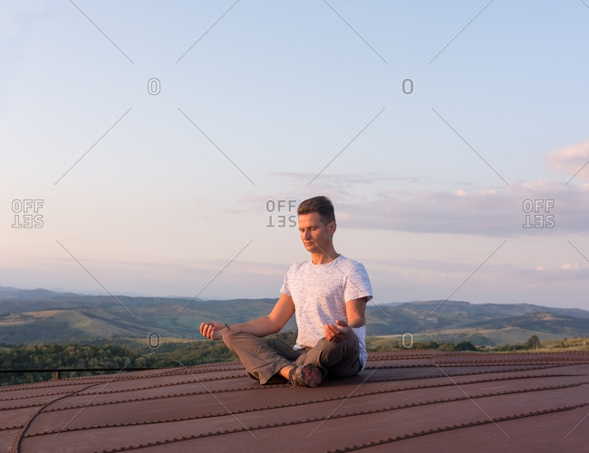 Adult man meditating on the terrace in the heat of the setting s