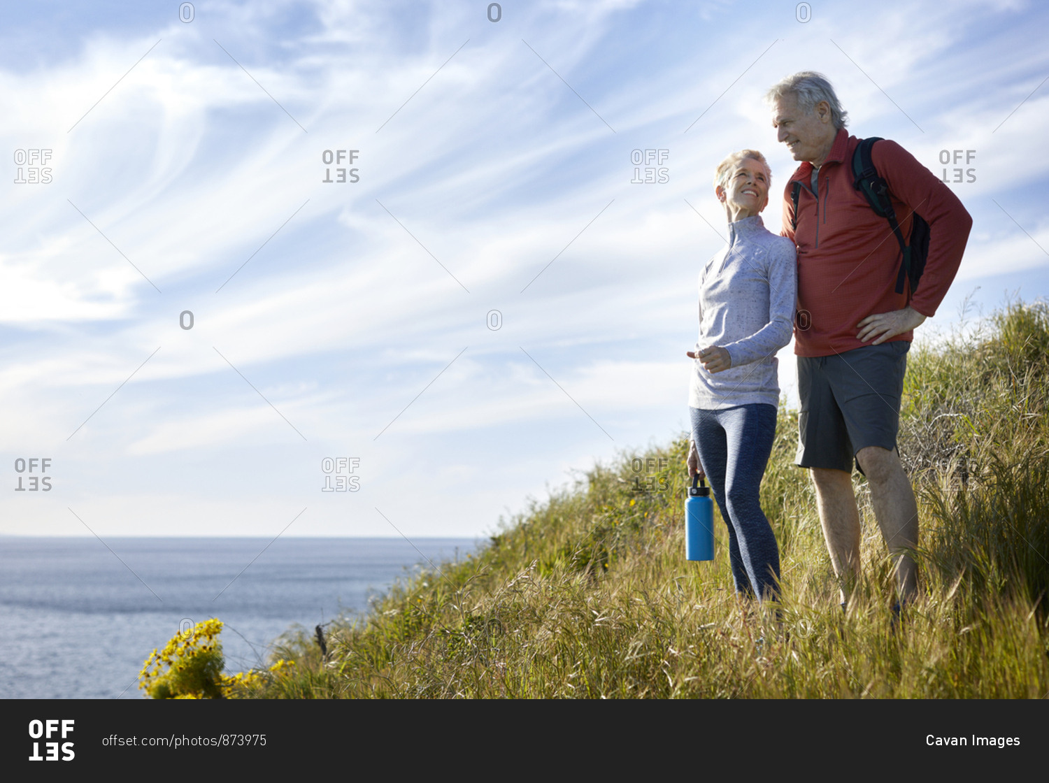 Smiling senior couple standing on cliff by sea against sky