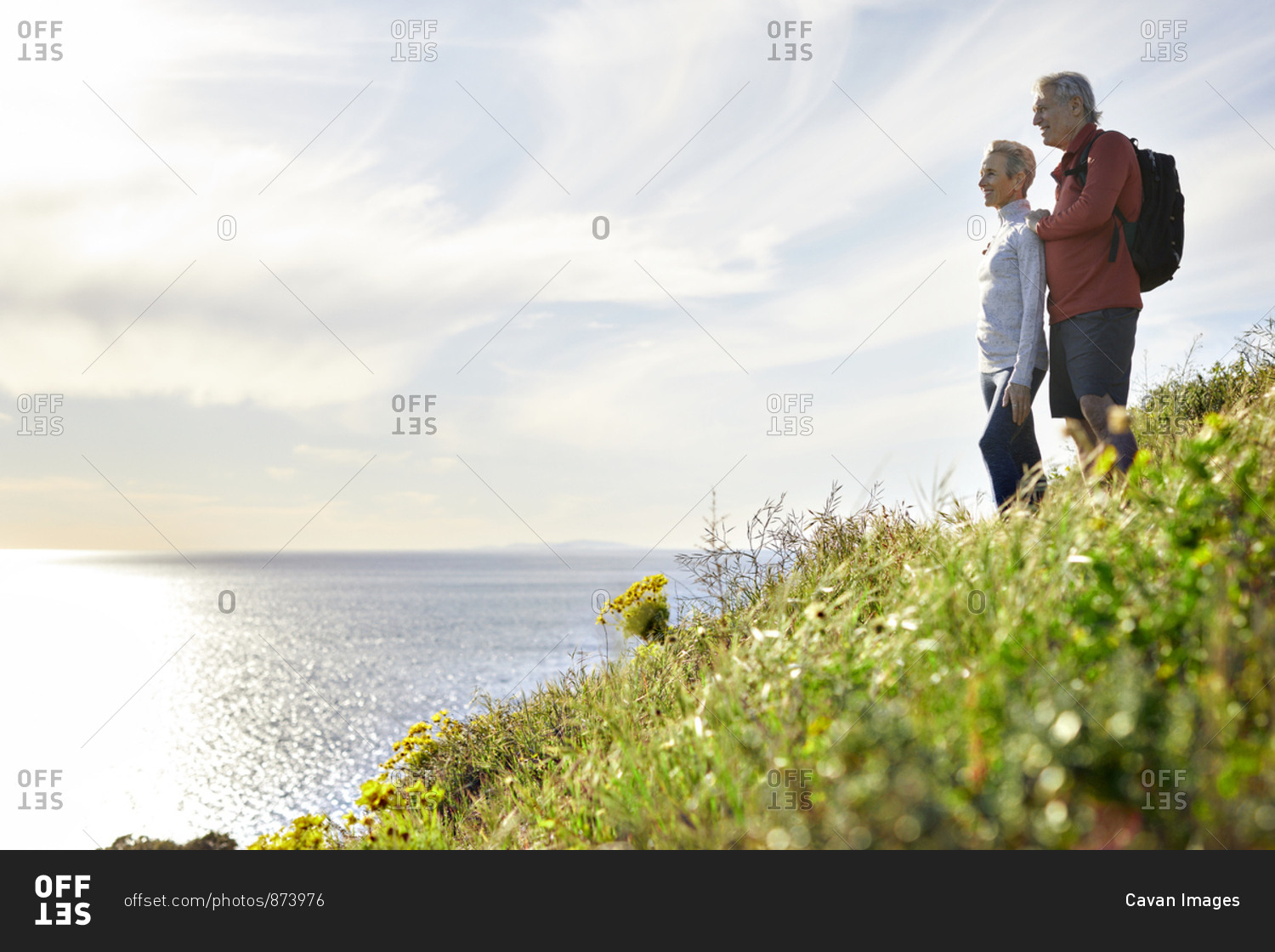 Side view of senior couple looking at sea while standing on cliff against sky
