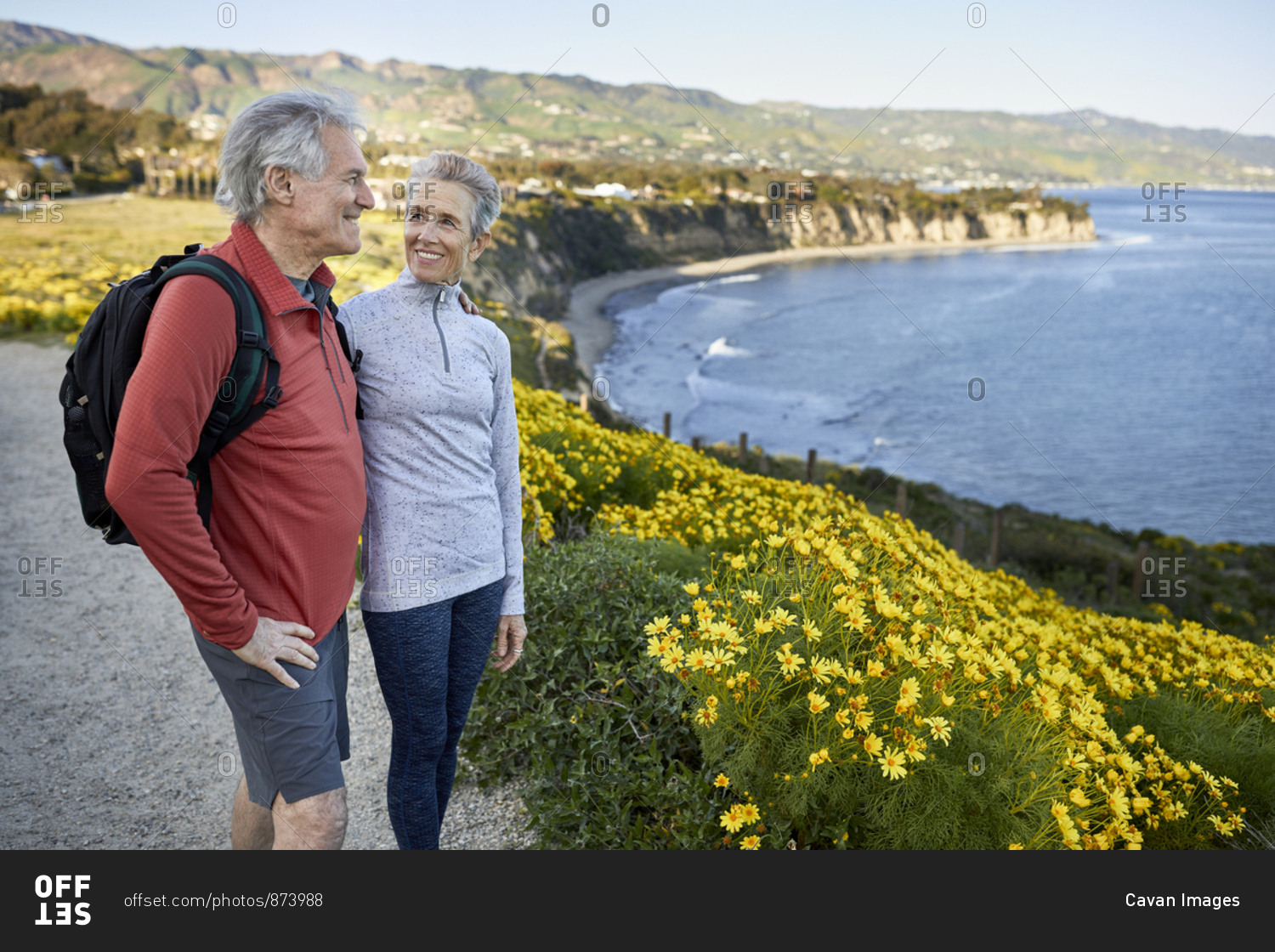 Smiling senior woman looking at man while standing by flowering plants on cliff at beach