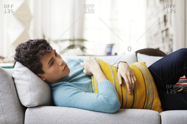 Thoughtful man holding cushion while lying on sofa at home