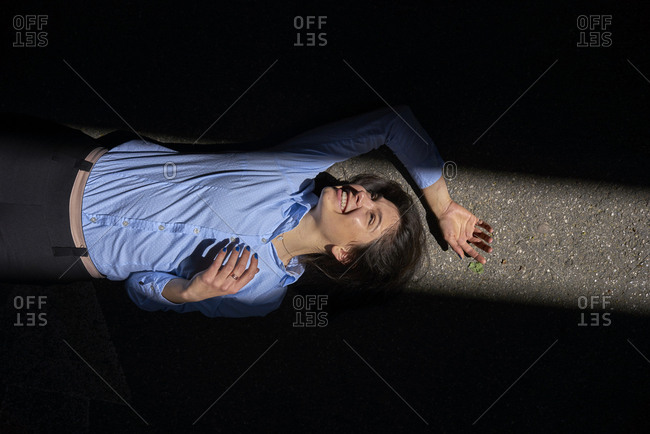 Laughing young woman lying between shadows and sunlight on the street