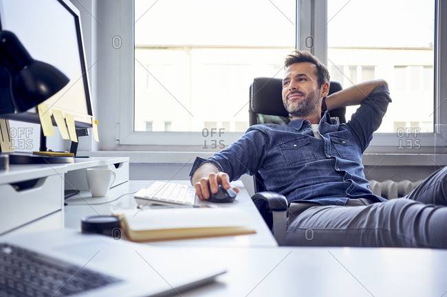 Relaxed man sitting at desk in office looking at computer screen