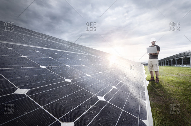 Engineer with laptop checking solar plant at evening twilight