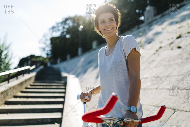 Smiling young woman with bicycle in backlight