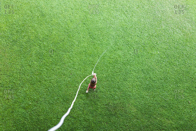 Little boy standing on lawn playing with garden hose- top view