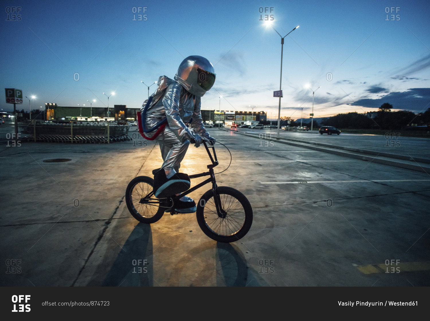 Spaceman in the city at night on parking lot riding bmx bike