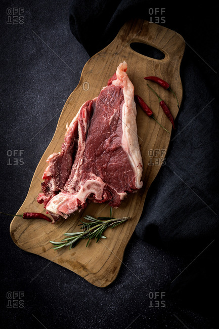 High angle view of beef with rosemary and red chili peppers on cutting board