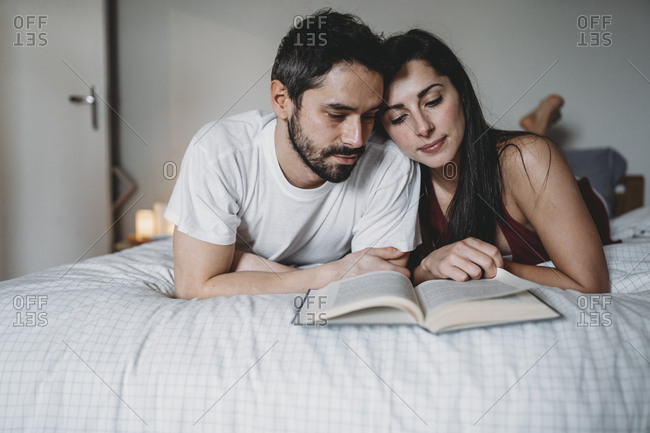 Loving couple reading a book in bed at home in a moment of relax stock  photo - OFFSET