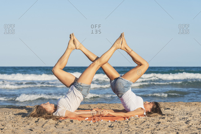 Two women practicing Acro Yoga on the beach stock photo - OFFSET