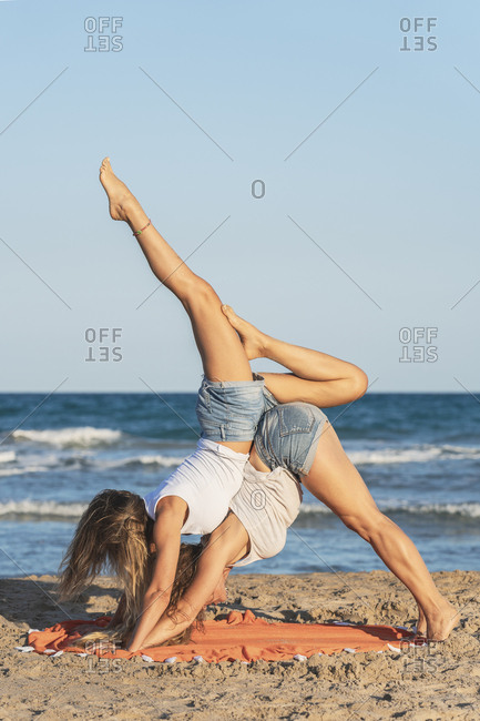 Two women practicing Acro Yoga on the beach stock photo - OFFSET