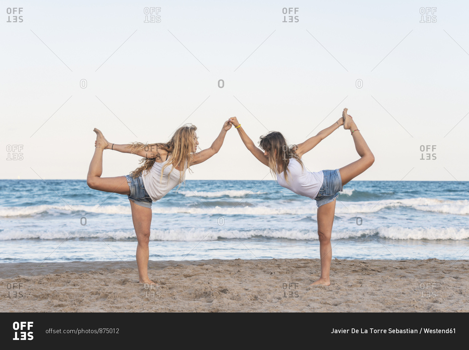 Two women practicing Acro Yoga on the beach stock photo - OFFSET