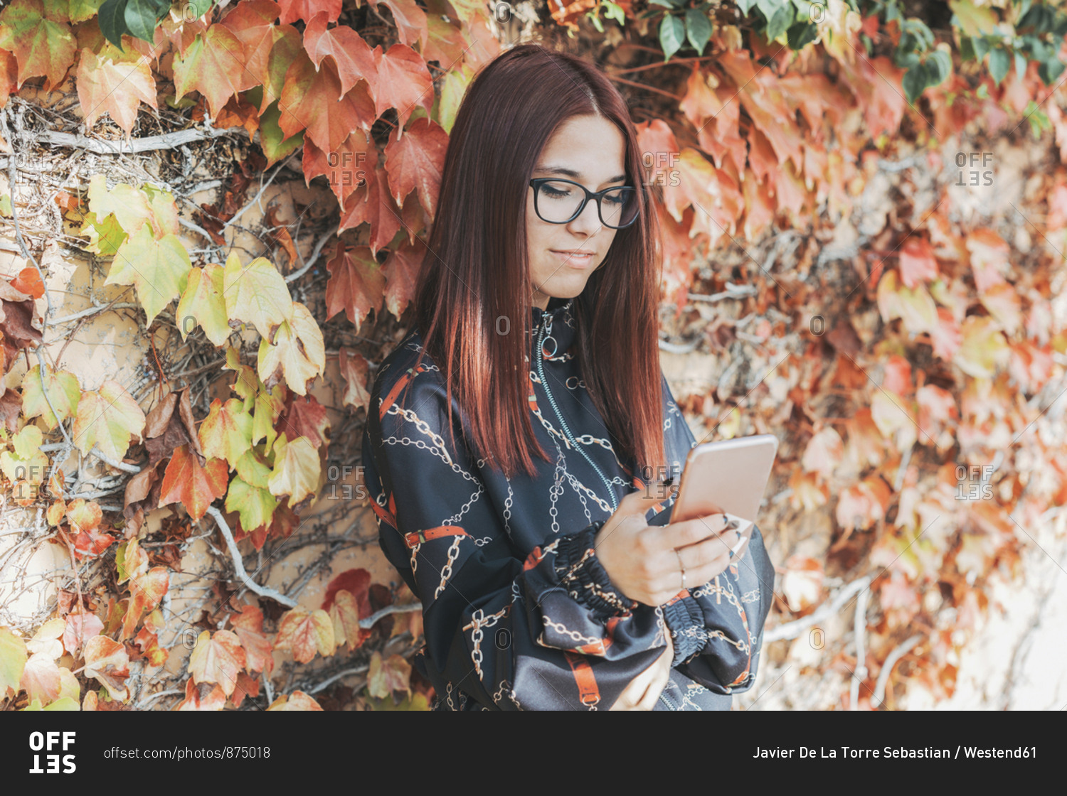Portrait of teenage girl with dyed red hair checking smartphone in autumn