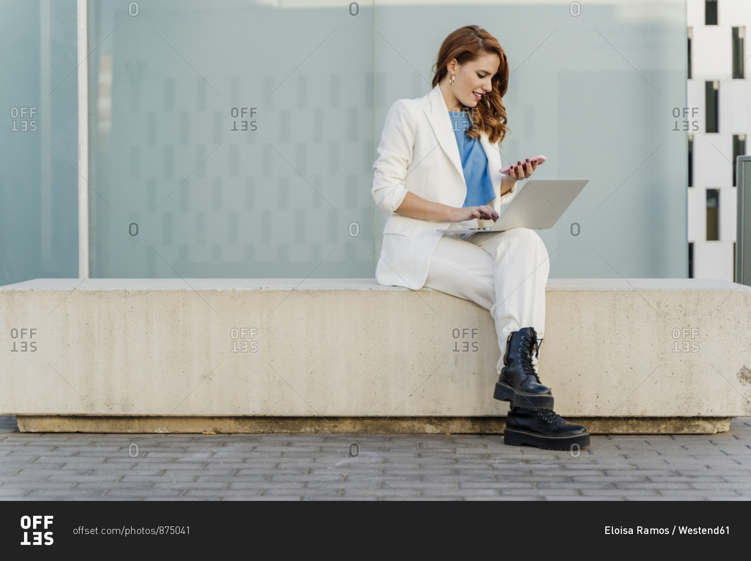 Businesswoman in white pant suit- sitting on bench- using laptop
