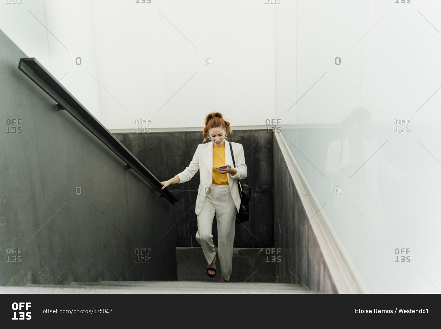 Businesswoman in white pant suit- ascending stairs- using smartphone