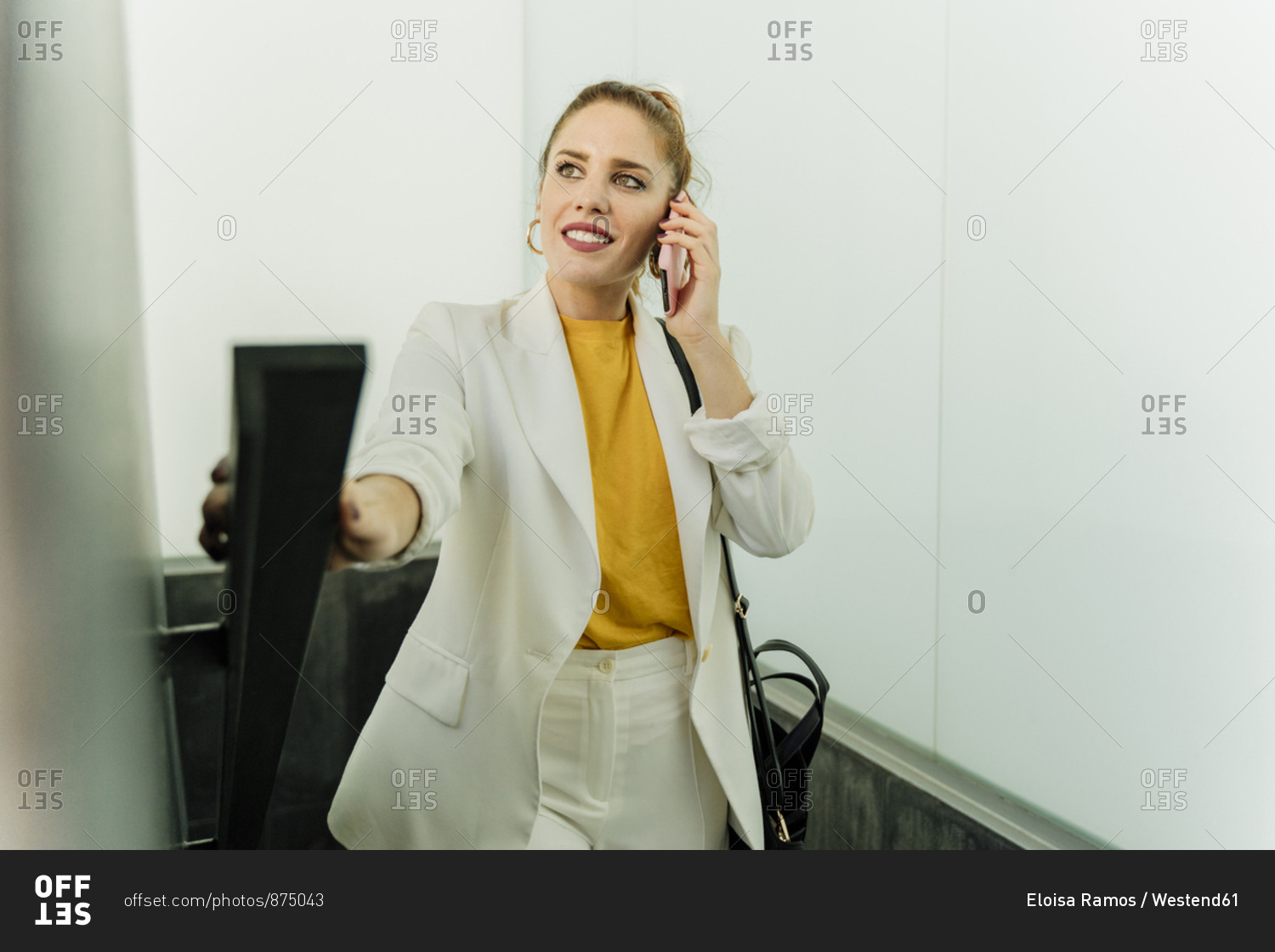 Businesswoman in white pant suit- ascending stairs- using smartphone