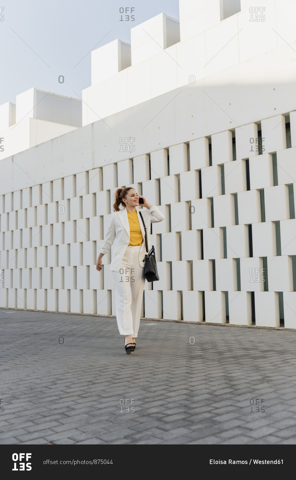 Businesswoman in white pant suit- walking in the city- talking on the phone
