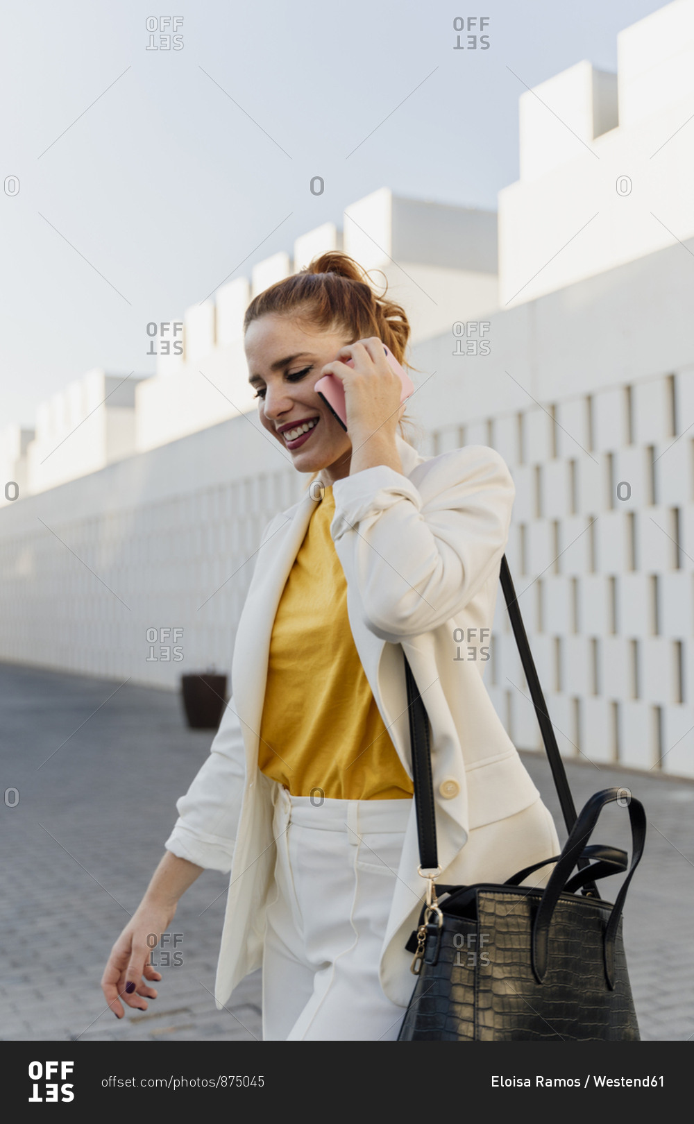 Businesswoman in white pant suit- walking in the city- talking on the phone