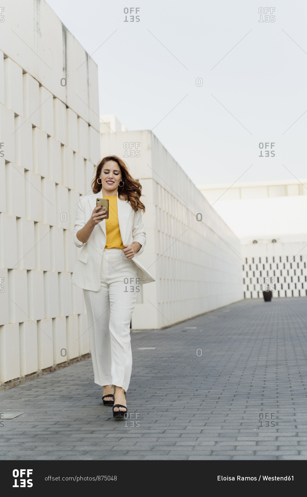 Businesswoman in white pant suit- walking in the city- using smartphone