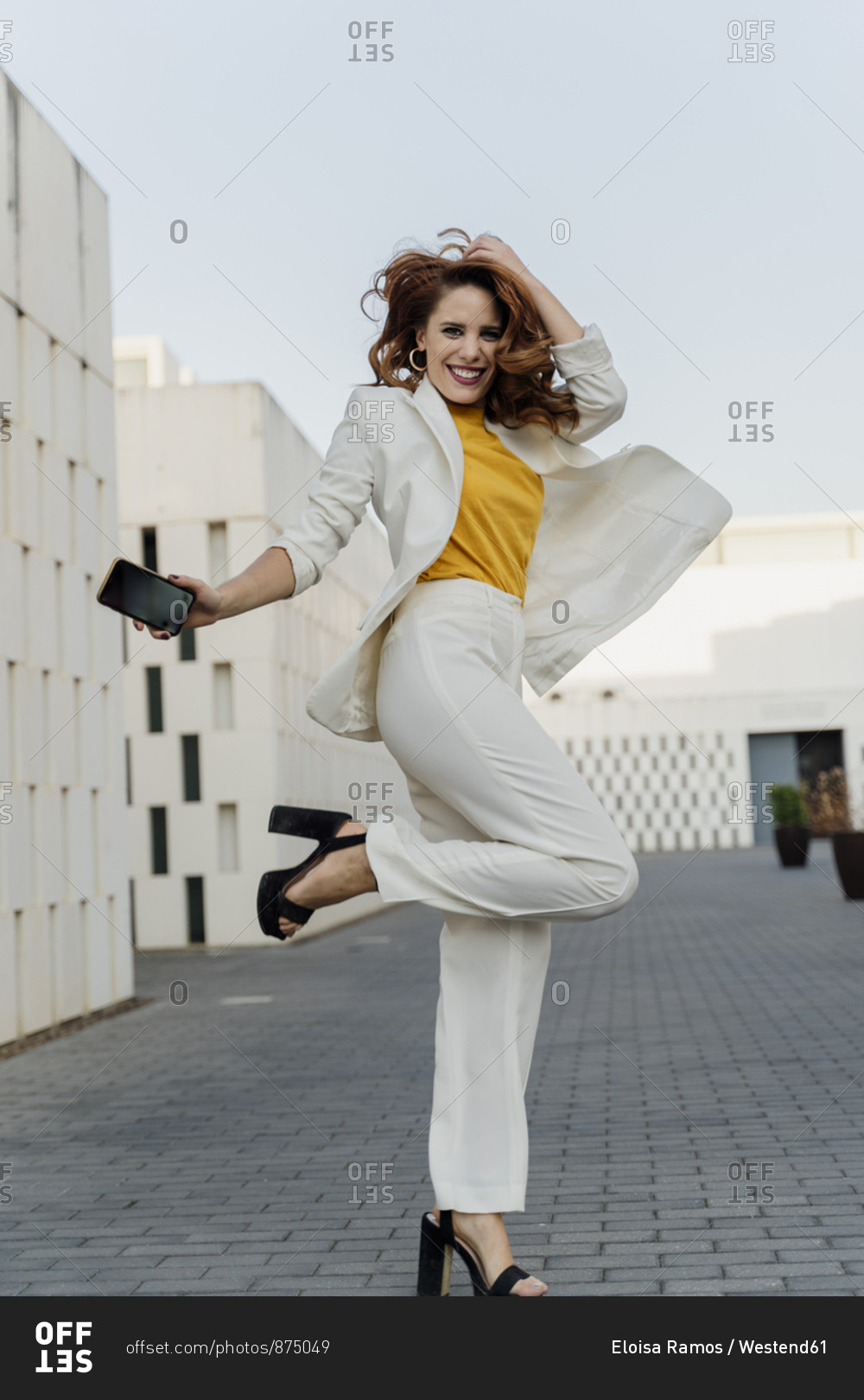Happy businesswoman in white pant suit- jumping and dancing in the street