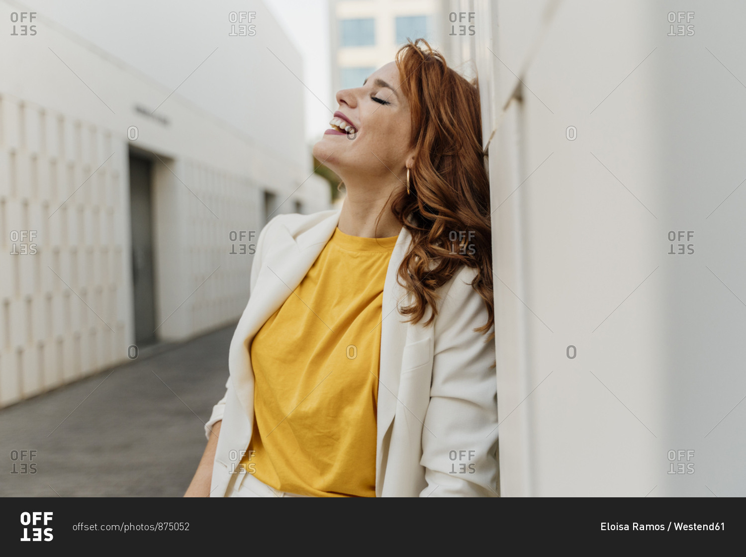 Beautiful businesswoman in white pant suit- leaning on wall- laughing