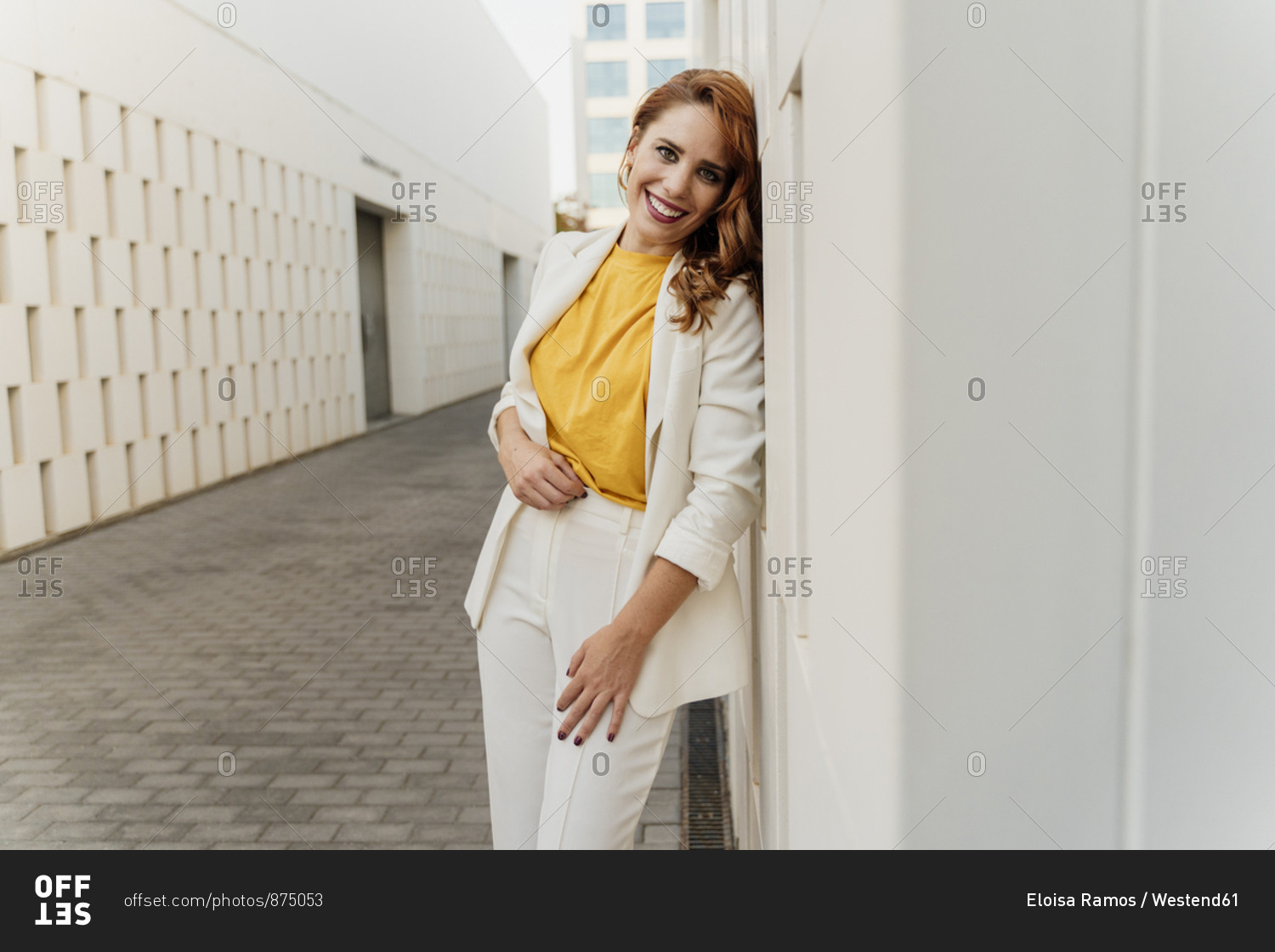 Beautiful businesswoman in white pant suit- leaning on wall- laughing