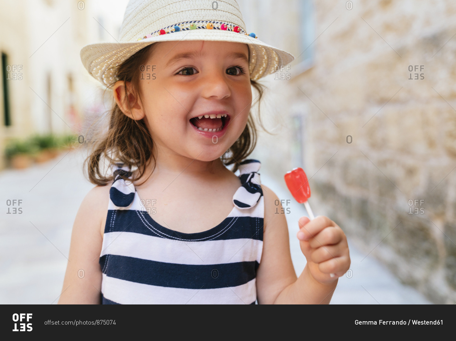 Portrait of happy little girl with red lollipop in summer