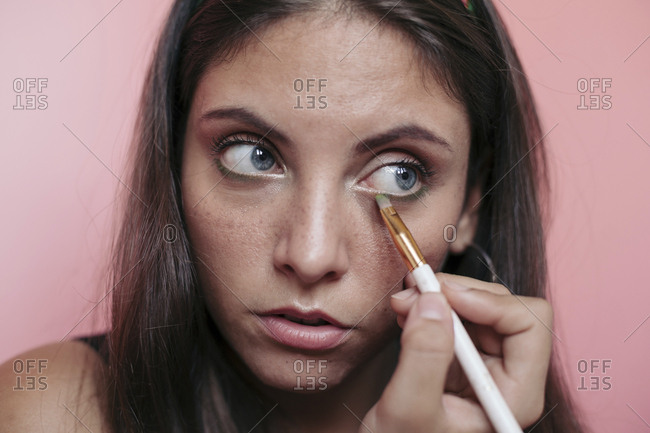 Close up of a young brunette woman with beautiful blue eyes applying eyeshadow with an eye brush