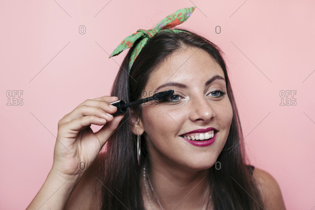 Young woman applying eyelash serum and smiling