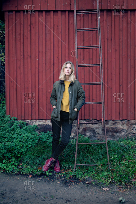 Blonde woman leaning on ladder that is propped on a red barn