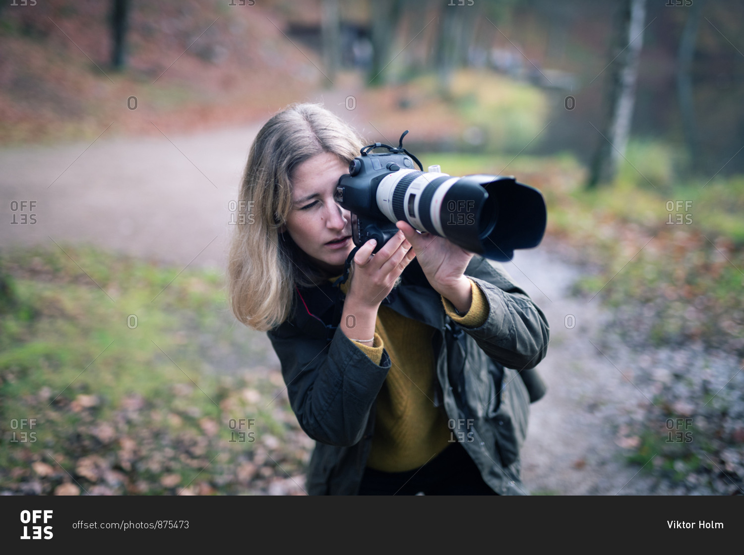 Blonde photographer using camera with large telephoto lens while taking shots in nature