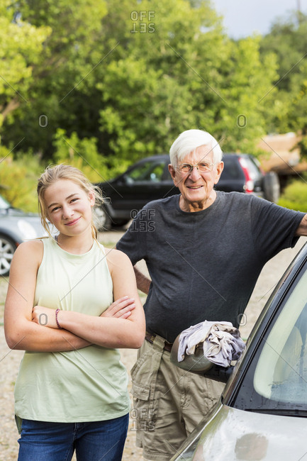 Senior man, grandfather and his 13 year old grand daughter washing a car together in driveway