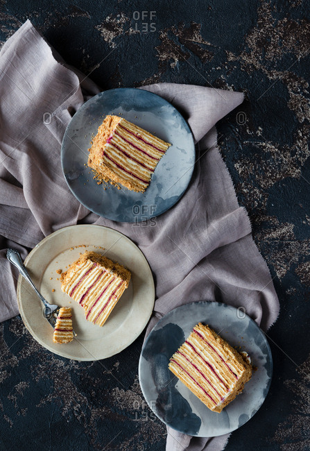 Slices of layered honey cake on plates over dark backdrop Russian Medovik cake top view
