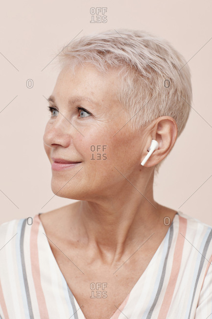 Modern mature woman wearing wireless earphones looking away vertical portrait