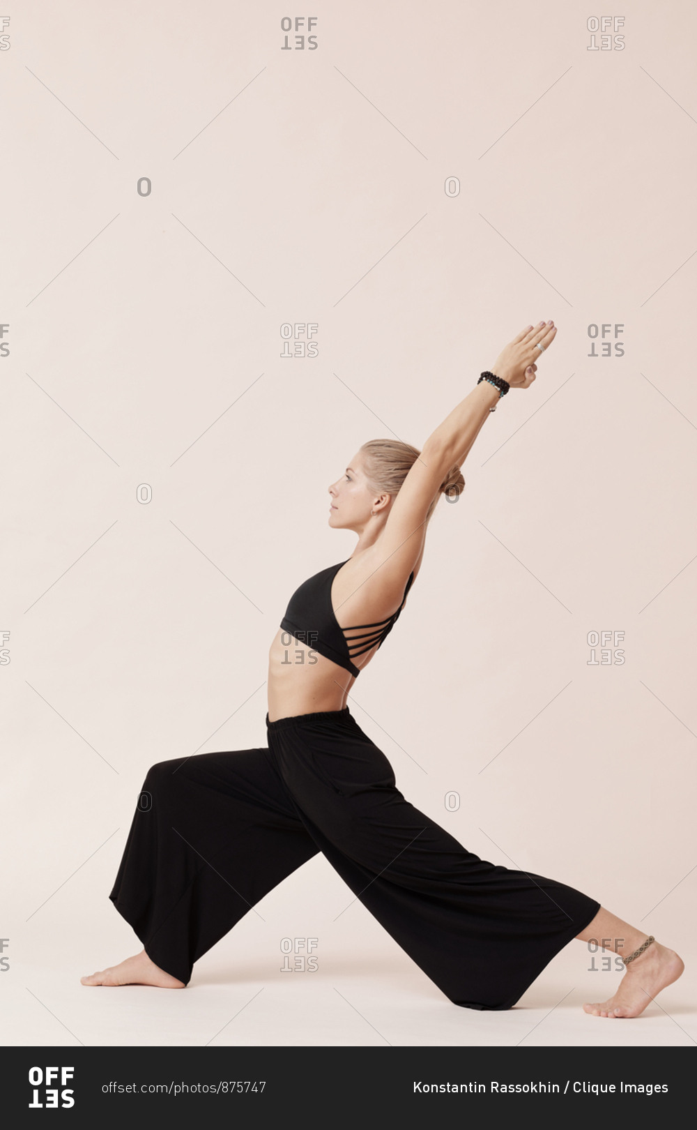 Good-looking young woman wearing black outfit practicing high lunge asana studio shot