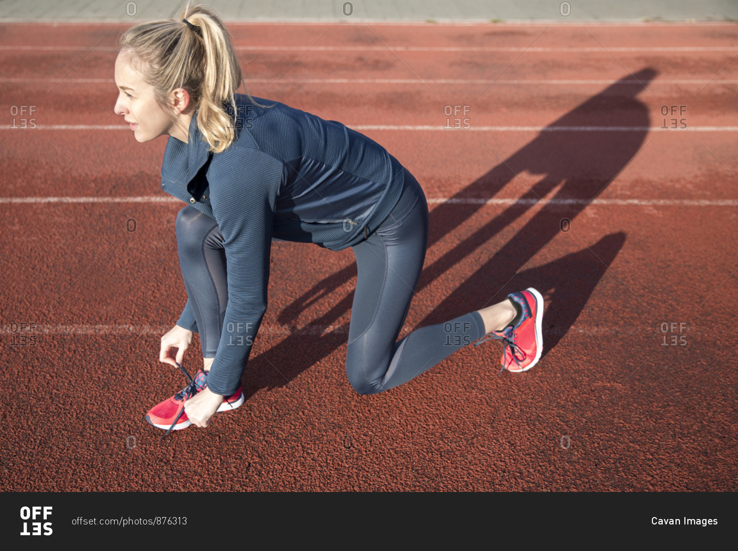 Side view of female athlete tying shoelace on sports track