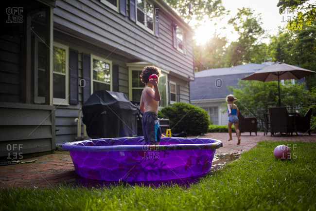 Girl Running While Brother Standing In Wading Pool At Backyard