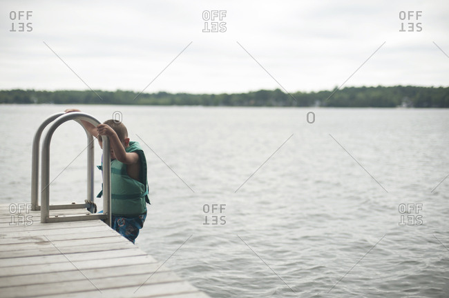 Boy climbing ladder of jetty against sky