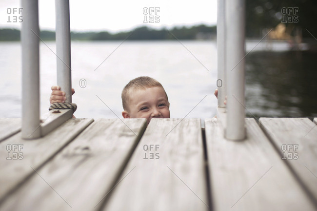 Portrait of happy boy climbing ladder of jetty against sky