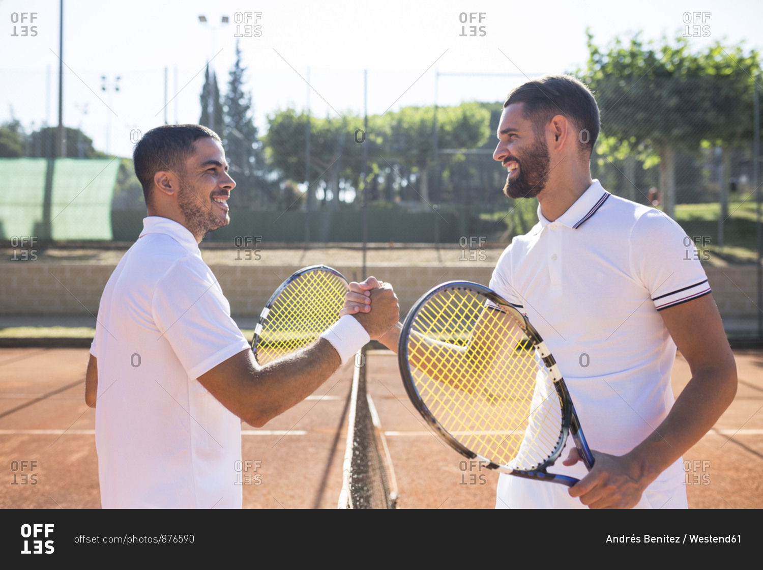 Side view of two tennis players with rackets shaking hands and smiling before tennis match