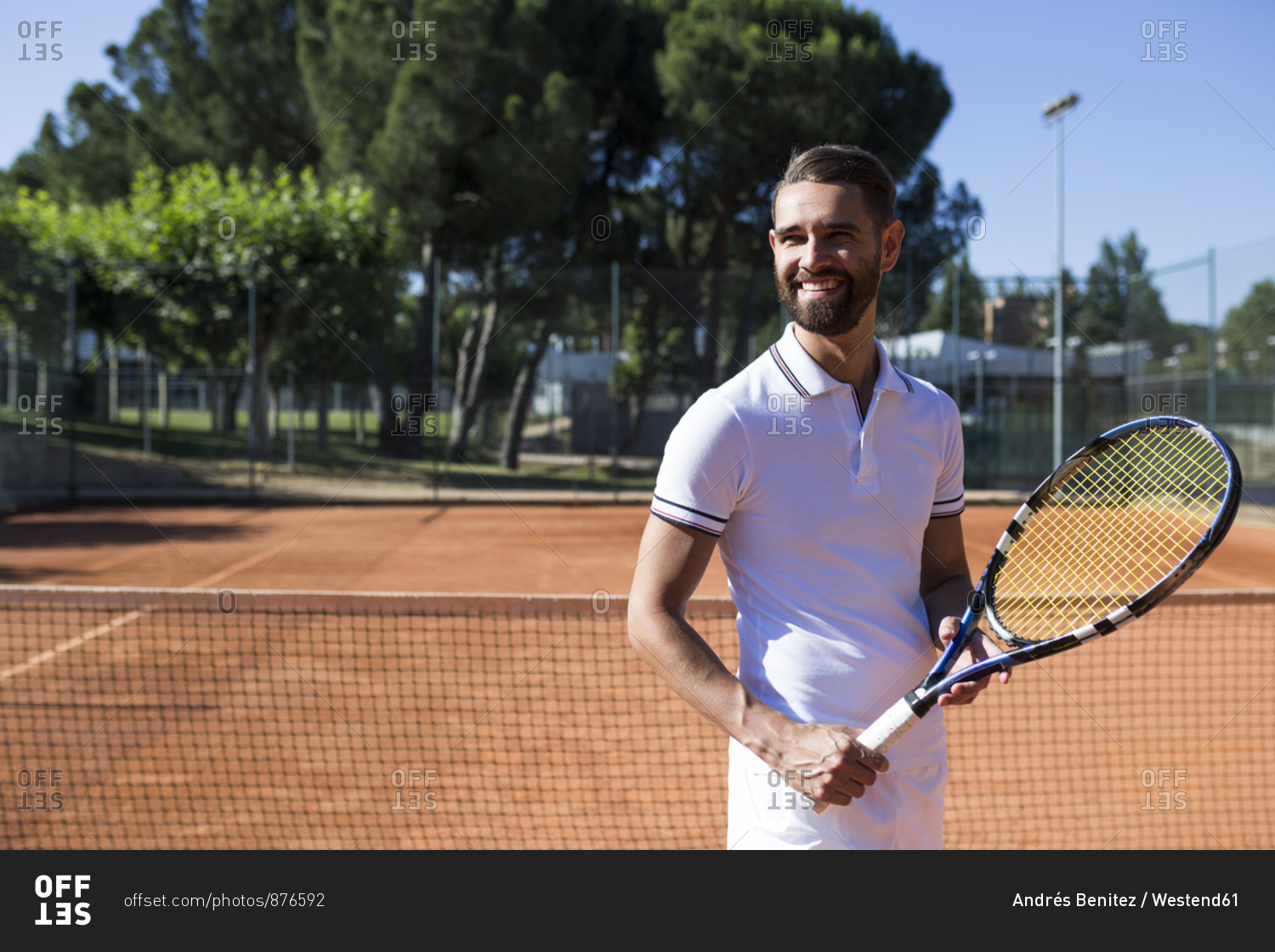 Attractive bearded man in tennis wear holding racket and looking away