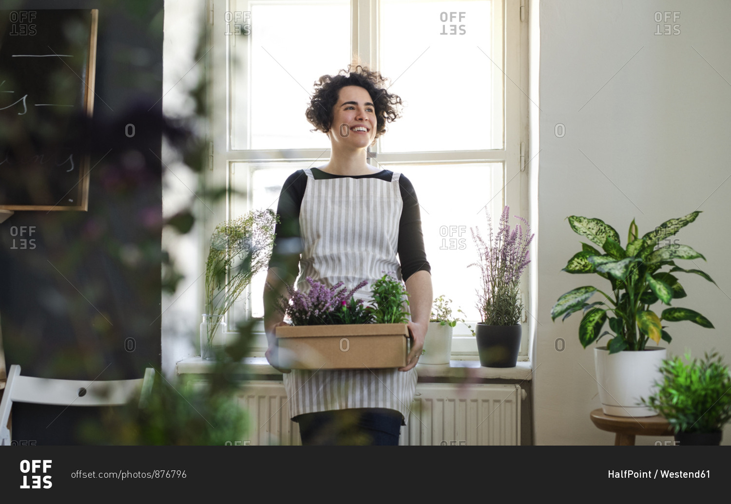 Happy young woman holding flowers in a cardboard box in a small shop