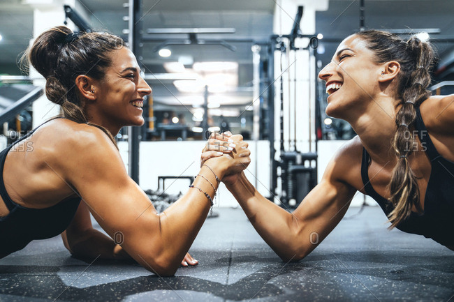 Happy female twins in good shape doing arm wrestling challenge in a gym