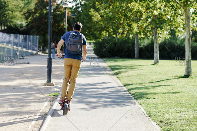 Back view of man with backpack riding electric scooter
