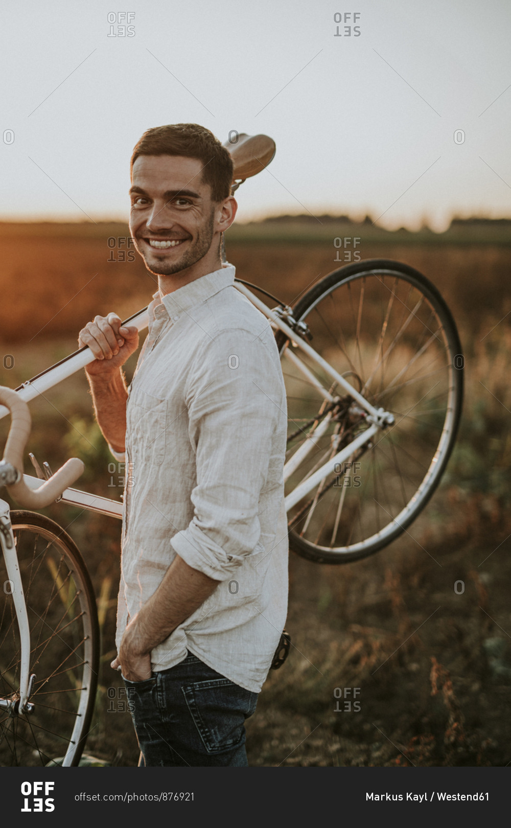 Portrait of a smiling young man carrying a racing cycle in the sunshine