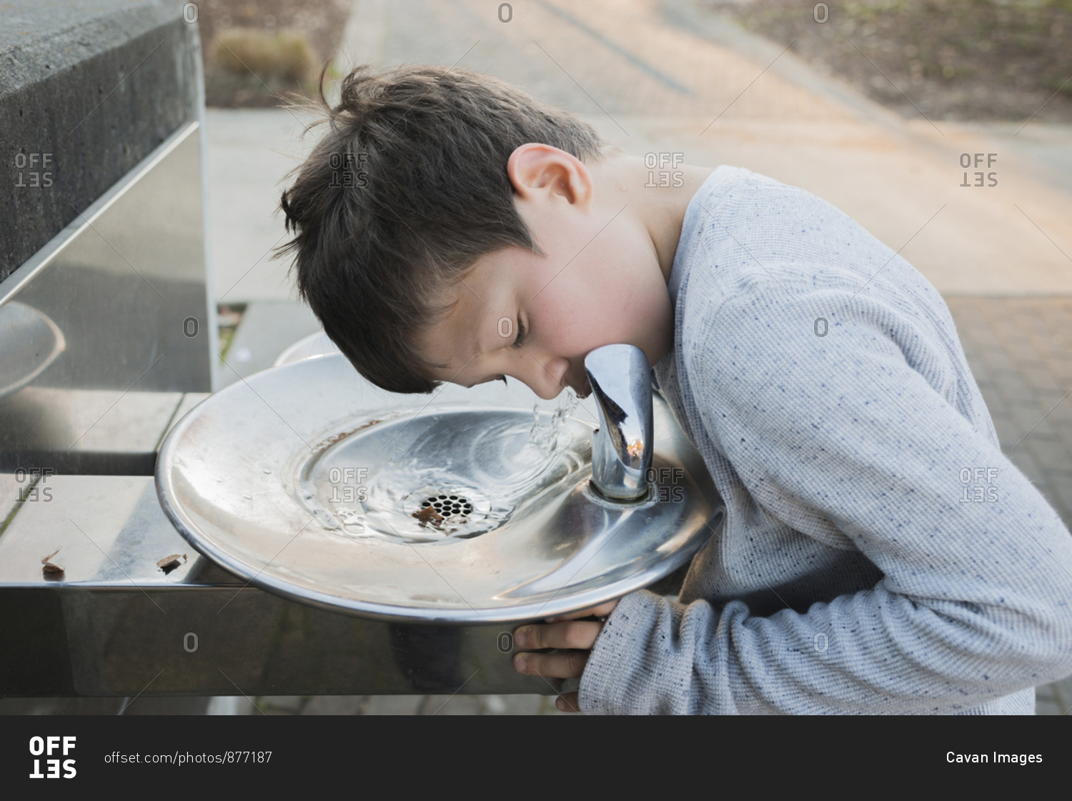 Thirsty boy drinking water from fountain at park